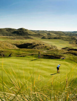 Family enjoying a round of golf on a lush green course near the beach at River Island Hotel.