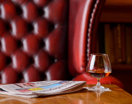 Cosy hotel lounge with newspaper and brandy glass on a wooden table.