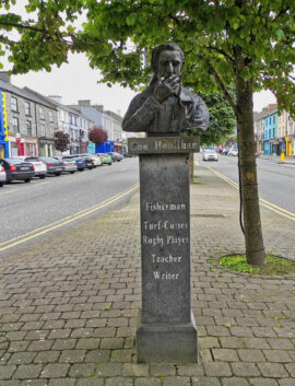 Bust sculpture of Con Houlihan under trees on a cobblestone street in Castleisland, Kerry.