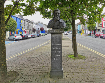 Bust sculpture of Con Houlihan under trees on a cobblestone street in Castleisland, Kerry.