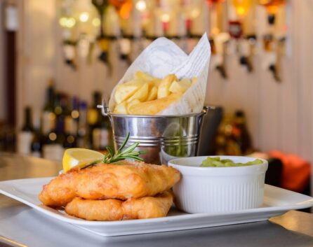 A plate of fish and chips with mushy peas in a cosy hotel restaurant.