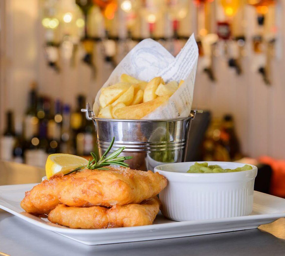 A plate of fish and chips with mushy peas in a cosy hotel restaurant.