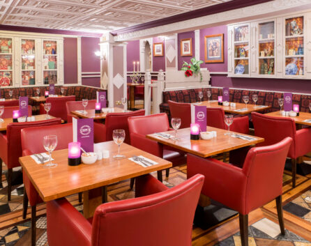 Cosy hotel dining room with red chairs, set for family meals, warm lighting.