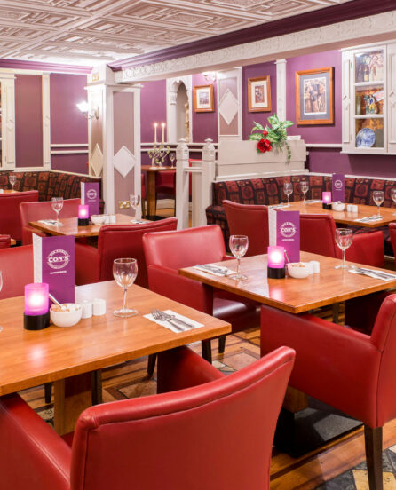 Cosy hotel dining room with red chairs, set for family meals, warm lighting.
