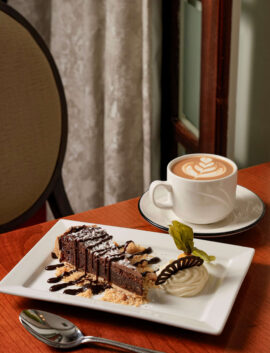 Chocolate dessert and cappuccino on a wooden table in cosy hotel cafe setting.