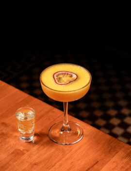 A refreshing passion fruit cocktail and a sparkling shot on a wooden table at River Island Hotel.