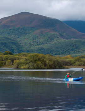 A family kayaking on a serene lake with lush mountains in the background near River Island Hotel.