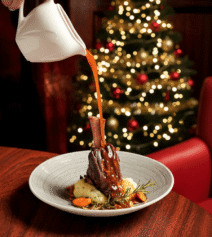 Festive lamb shank dinner in cosy hotel setting with Christmas tree.