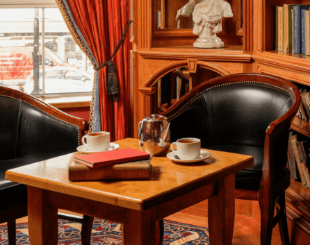 Cosy hotel lounge with books, armchairs, and tea set; ideal for relaxation.