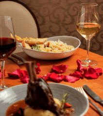 Cosy dining setup at River Island Hotel with pasta, lamb, wine, and rose petals on a table.
