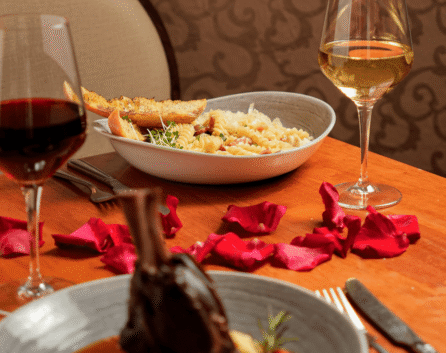 Cosy dining setup at River Island Hotel with pasta, lamb, wine, and rose petals on a table.