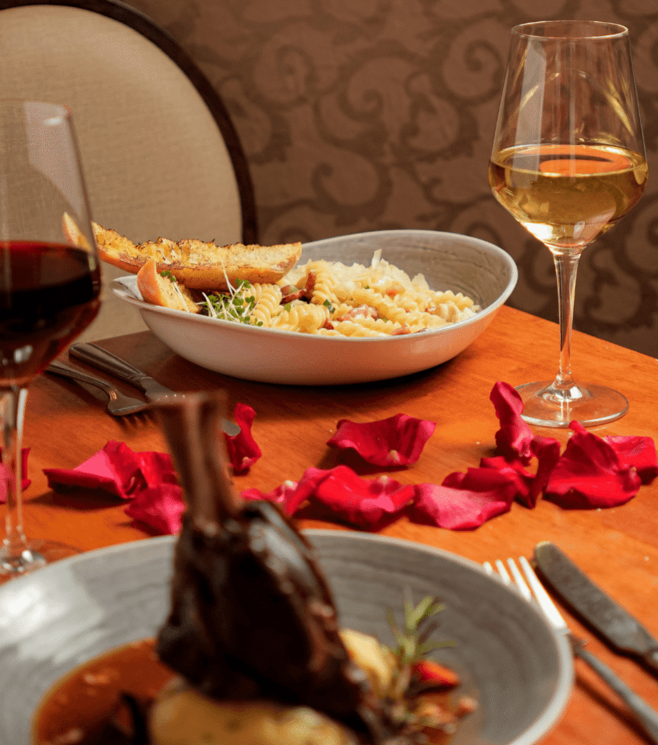 Cosy dining setup at River Island Hotel with pasta, lamb, wine, and rose petals on a table.