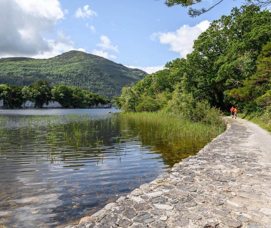 Family walking by a serene lake with mountain view at River Island Hotel, Kerry.