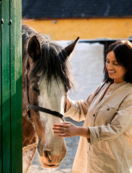 Smiling woman gently strokes a horse at River Island Hotel's stable outdoors.