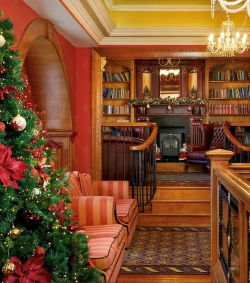 Festive hotel lounge with Christmas tree and cosy seating near a fireplace.
