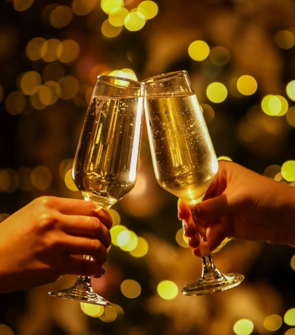 Two people clinking champagne glasses in a festive, warmly lit hotel setting.