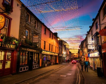 A lively street at dusk near River Island Hotel, lit with string lights, with families exploring shops.