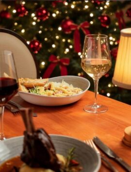 Festive dining at River Island Hotel with lamb shank, pasta, and wine near a glowing Christmas tree.