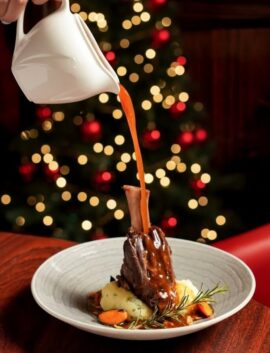 Festive dinner setting with pouring sauce over lamb shank at River Island Hotel.
