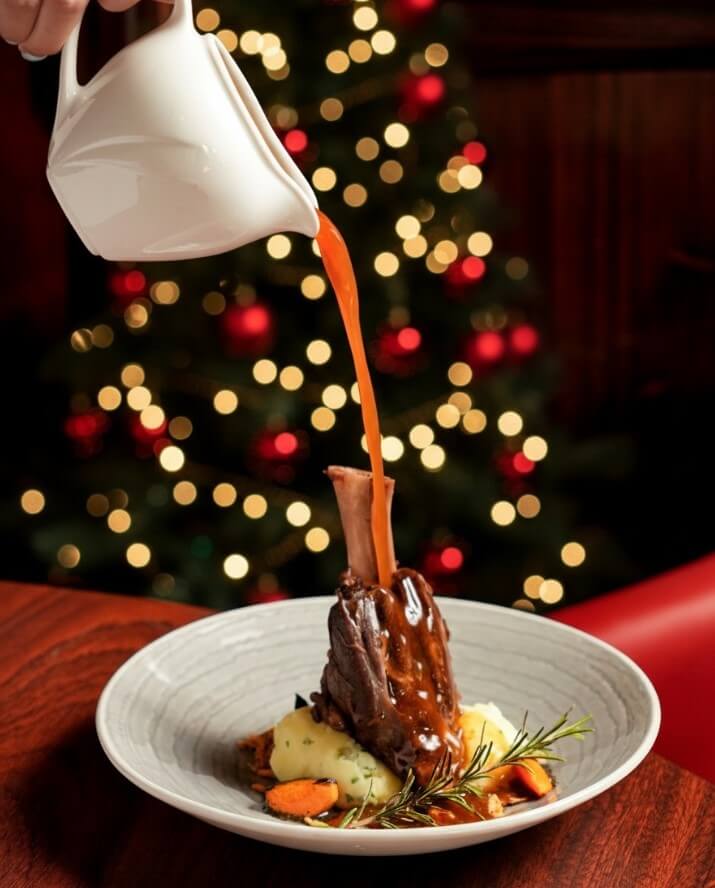 Festive dinner setting with pouring sauce over lamb shank at River Island Hotel.