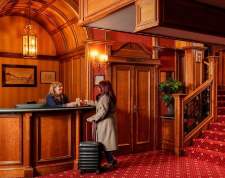 A guest checks into River Island Hotel at the warm, wooden reception. Luggage at their side.