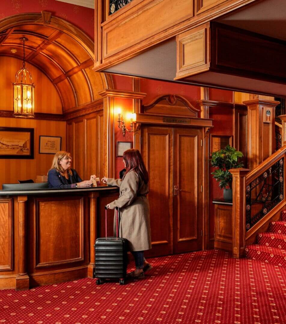 A guest checks into River Island Hotel at the warm, wooden reception. Luggage at their side.