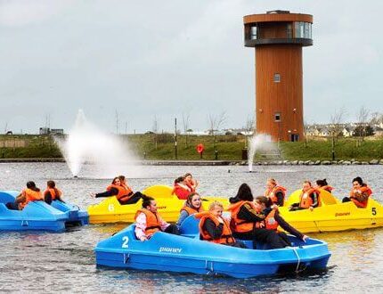 Diverse group enjoying pedal boating near River Island Hotel with watchtower in view.